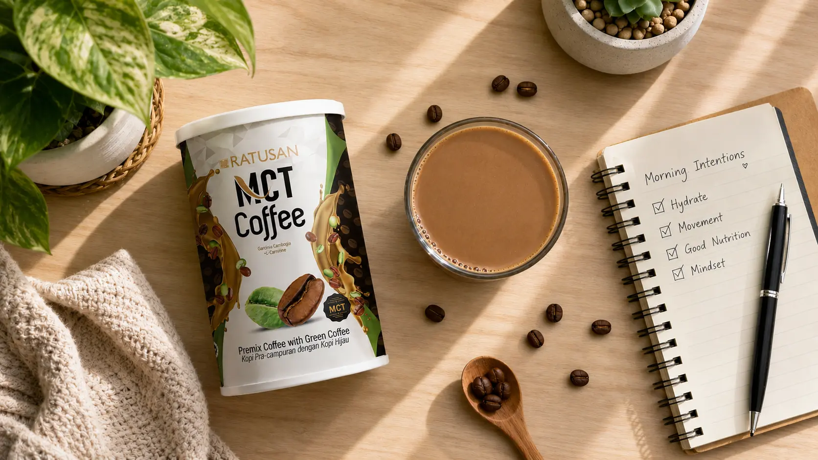 Overhead flat lay of a morning wellness routine with Ratusan MCT Coffee tin, coffee glass, beans and a journal on a wooden desk